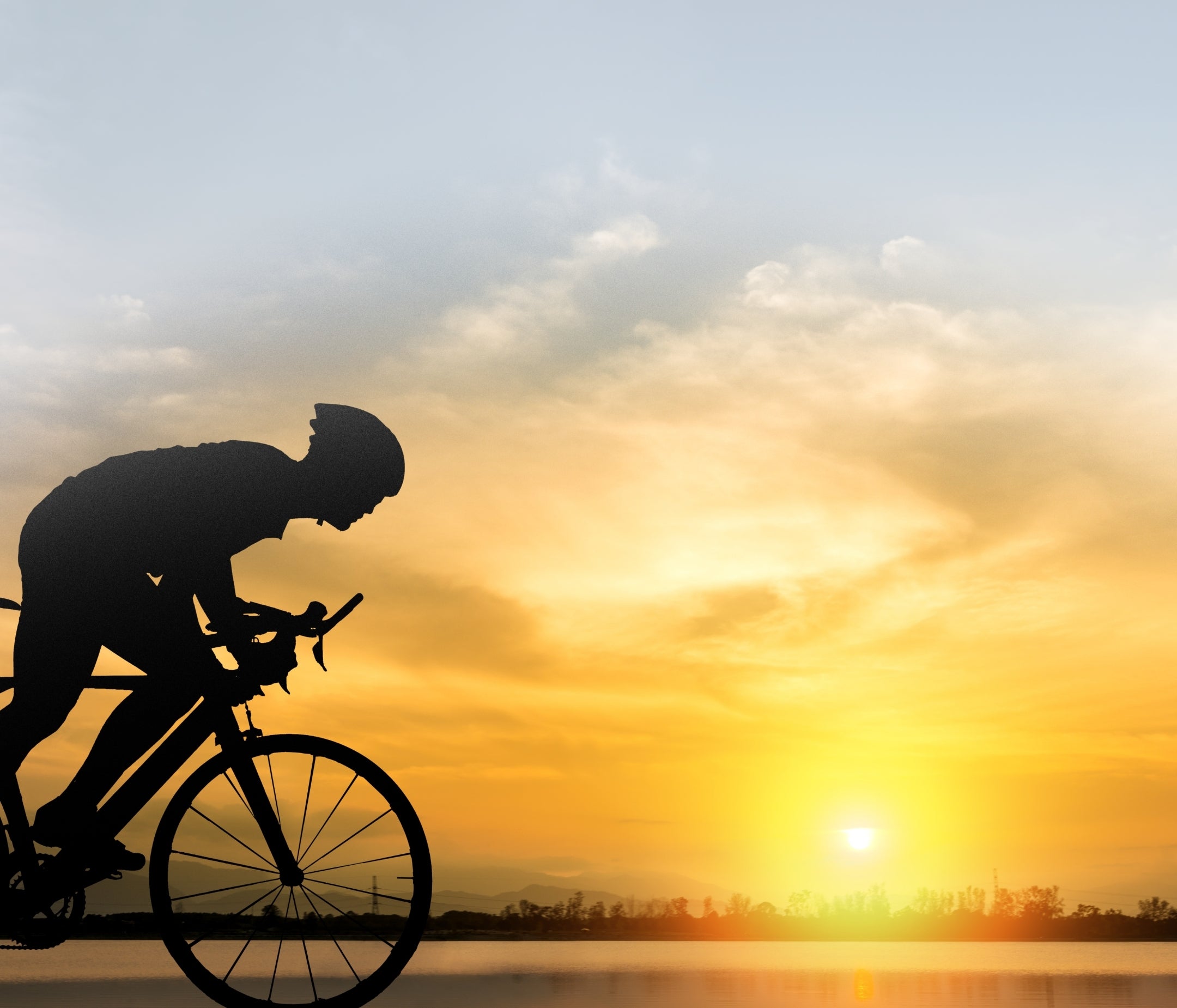 Silhouette of a cyclist against a sunset sky with a lake in the background