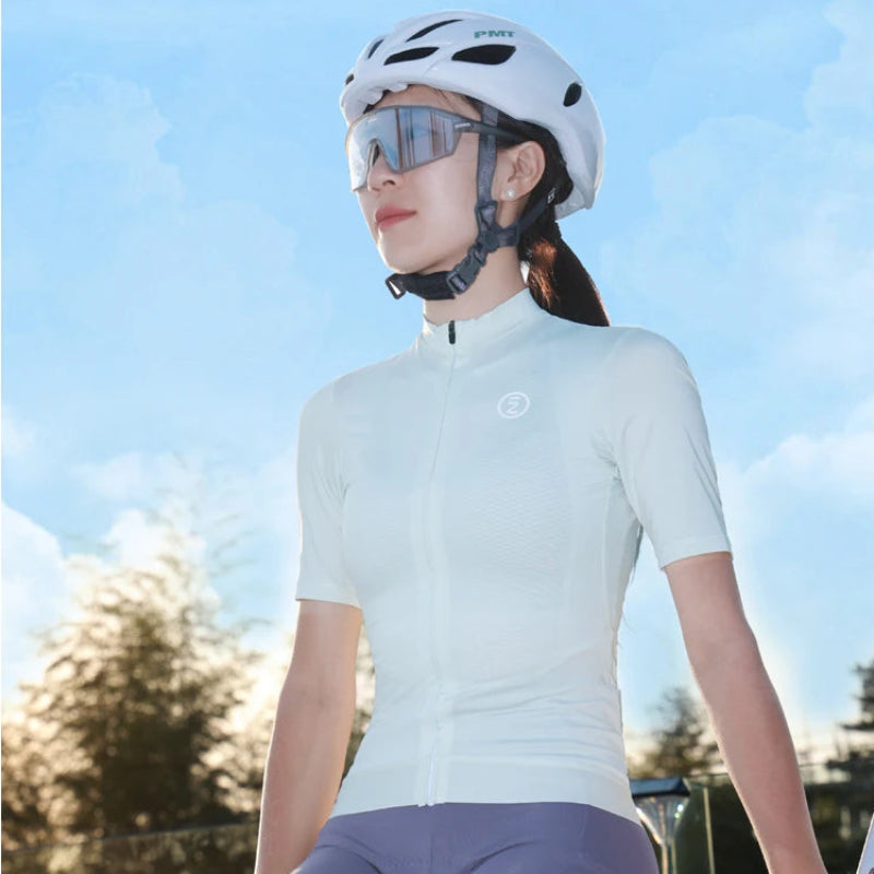 A woman wearing a white cycling jersey, matching white helmet, and reflective cycling sunglasses, sitting outdoors against a blue sky background.