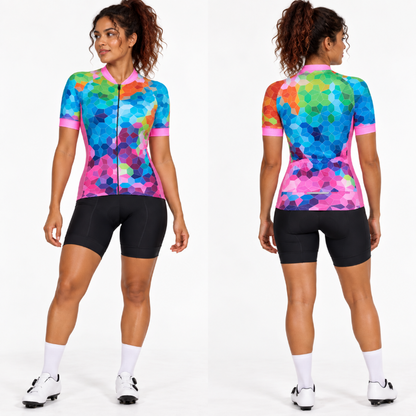 Front and back views of a woman modeling a short-sleeve cycling jersey with a colorful geometric hexagon pattern in blue, pink, purple, green, and orange, paired with black cycling shorts, white socks, and cycling shoes against a white studio background.