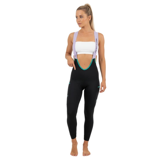 Woman wearing black leggings with a white sports bra and purple suspenders on a white background