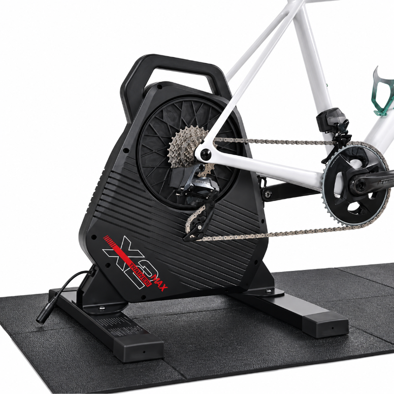 A black indoor cycling trainer with a white bicycle mounted on it, photographed on a clean white background. The trainer has red and white branding that reads 'X3' and 'SPECIALIZED MAX'.