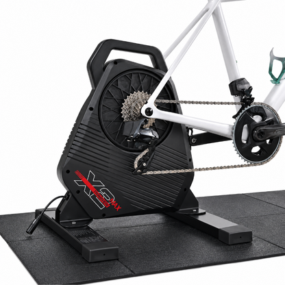 A black indoor cycling trainer with a white bicycle mounted on it, photographed on a clean white background. The trainer has red and white branding that reads 'X3' and 'SPECIALIZED MAX'.