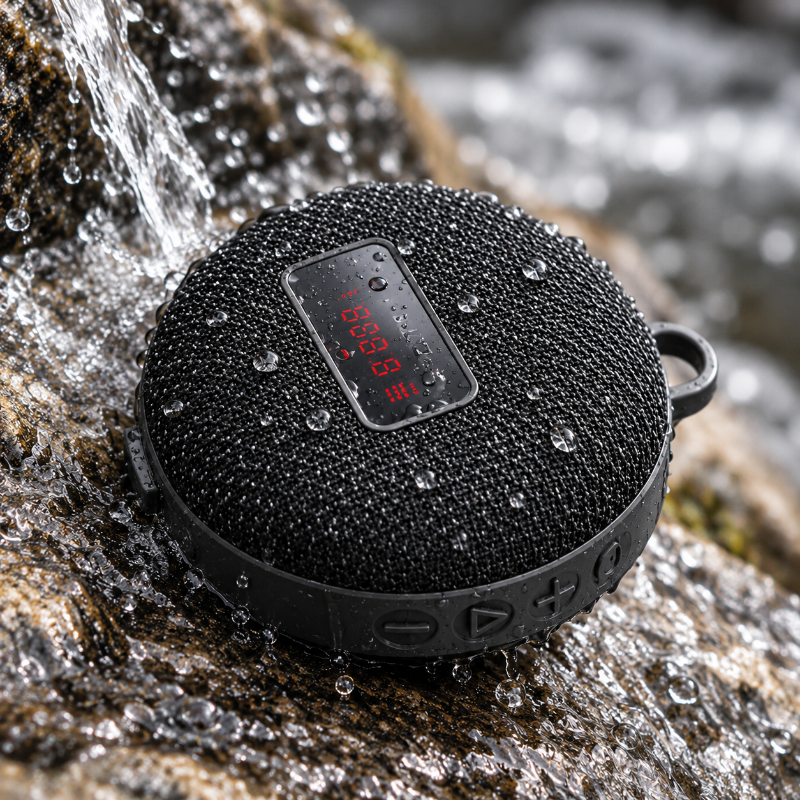 A black Portable Bluetooth Speaker for Bike waterproof speaker with a digital LED display, shown outdoors on a wet rock with water droplets and flowing water in the background.