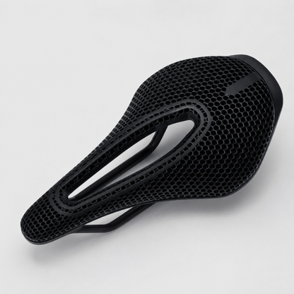 A black bicycle saddle with a textured honeycomb mesh pattern, shown from a three-quarters perspective on a light gray background.