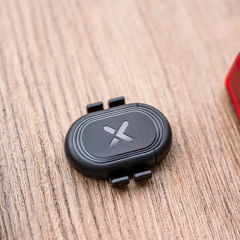 Black device with a logo on a wooden surface next to a smartphone and red light