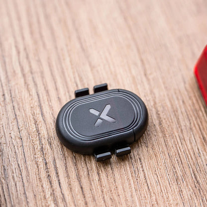 Black device with a logo on a wooden surface next to a smartphone and red light