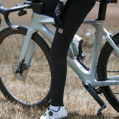 Person wearing black cycling pants with a visible brand logo, standing next to a bicycle in an outdoor setting.