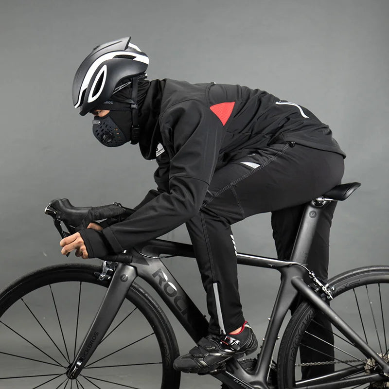 Person wearing a black helmet and black outfit with a red logo, riding a black bicycle on a gray background
