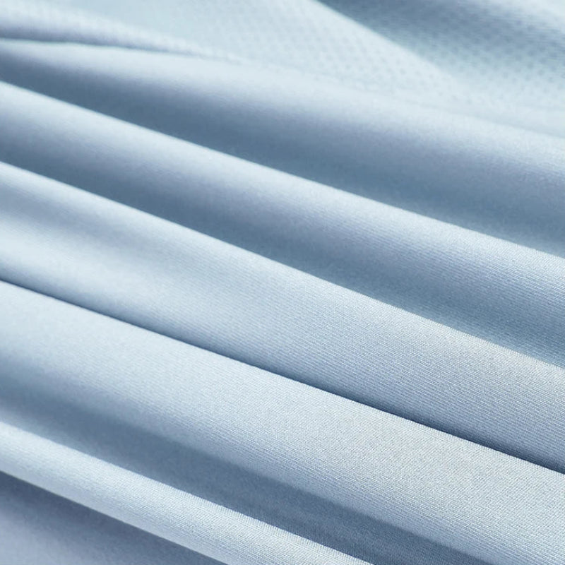 Light blue textured fabric with soft diagonal folds and pleats, shown in a close-up view.