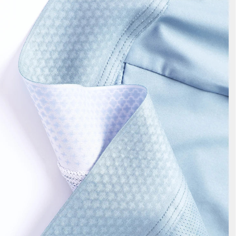 Close-up of a light blue garment, likely a scrub top or medical uniform, showing a textured geometric pattern on the fabric and a white mesh inner lining.