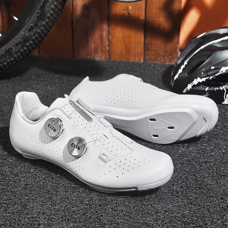 White cycling shoes with 'Cru' branding on a textured surface with a helmet and bike tire in the background.