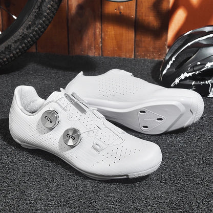 White cycling shoes with 'Cru' branding on a textured surface with a helmet and bike tire in the background.