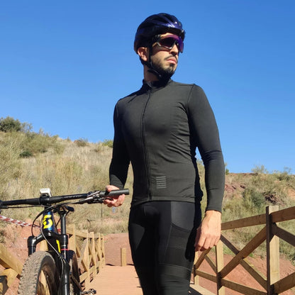 Man in cycling gear standing next to a mountain bike on a trail with a clear blue sky.