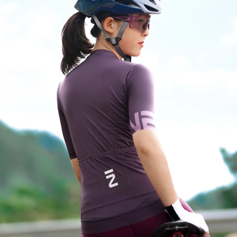 Person wearing a purple cycling outfit with a helmet and sunglasses, riding a bike outdoors.